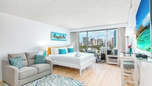 A modern hotel room with a bed, sofa, desk, and large windows offering a city view.