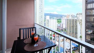 A balcony with a table and two glasses of orange juice, overlooking a cityscape with tall buildings.