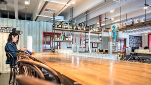 A bar area with wooden tables and chairs, a bar counter, shelves with bottles, and a sign reading "WELCOME TO RACIN' KITCHEN."