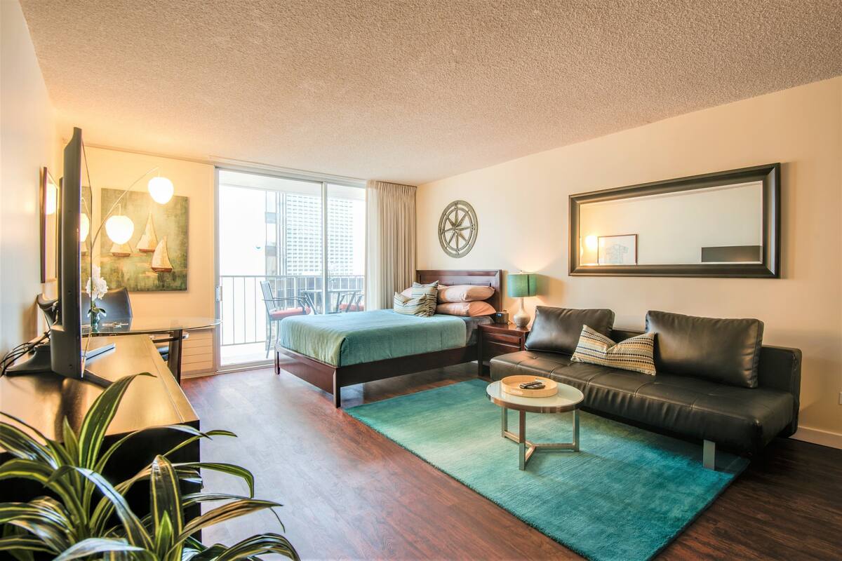 A modern bedroom with a bed, a desk, a sofa, and a balcony with a view.