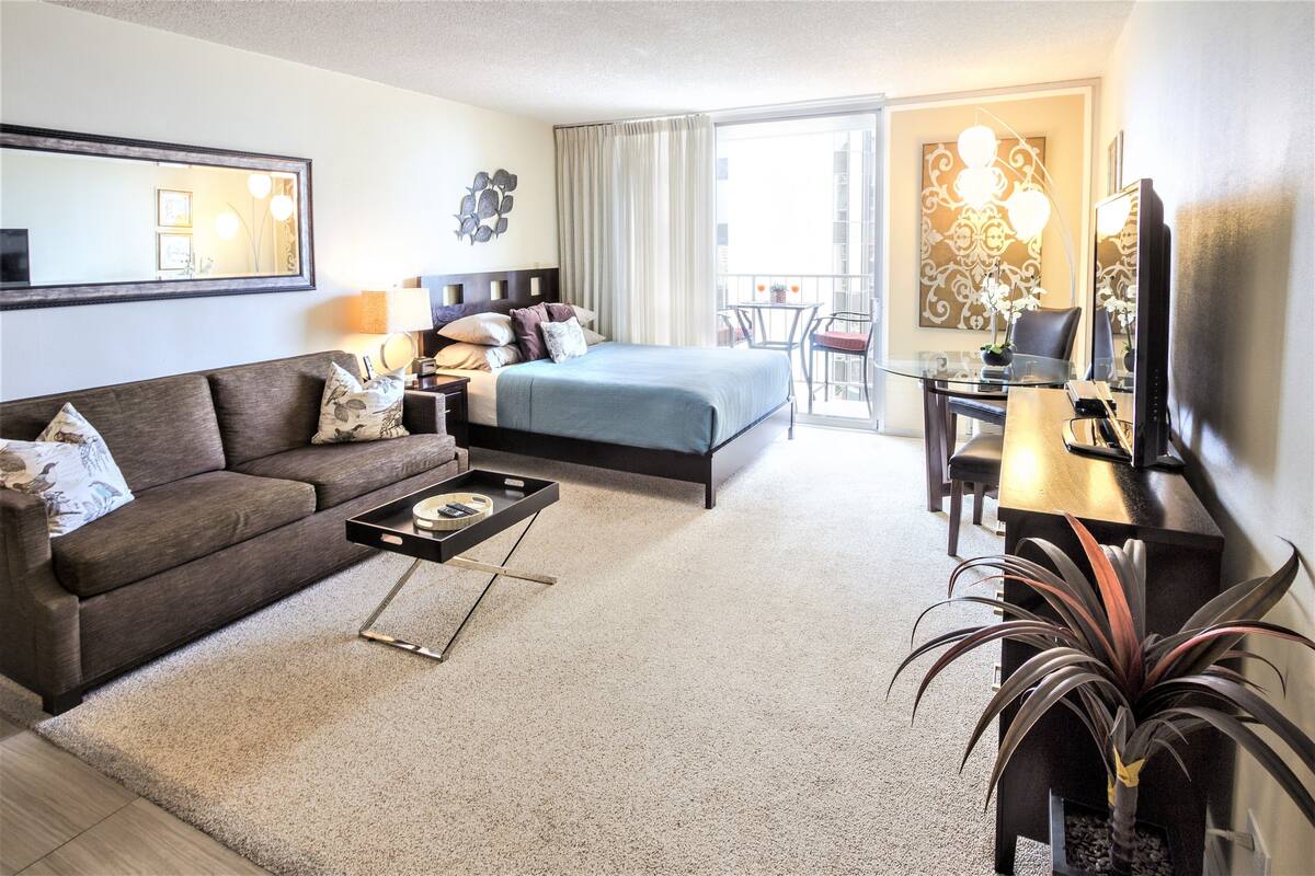 A modern hotel room with a bed, sofa, desk, and balcony.