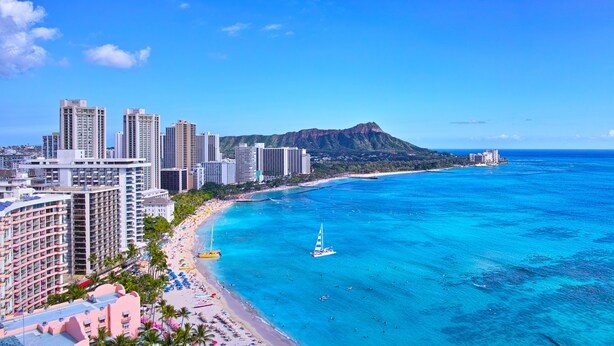 A coastal cityscape with high-rise buildings, a beach, and a mountain in the background.