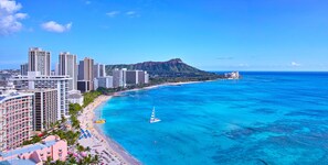Un paisaje costero con edificios altos, una playa y una montaña al fondo.