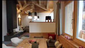 A cozy living room with a wooden dining table, comfortable seating, a fireplace, and a large window with a view. - Chalet Binna (Zermatt)