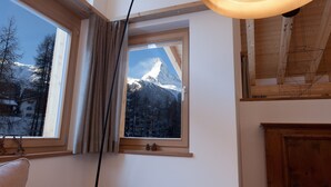 A cozy room with a large window overlooking a snowy mountain, a wooden ceiling, and a modern lamp. - Chalet Binna (Zermatt)