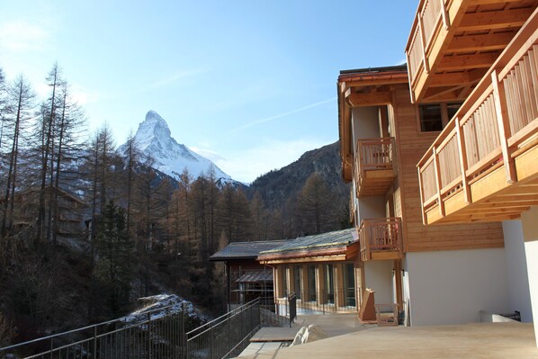 A wooden building with a balcony, a mountain in the background, and a forested area.