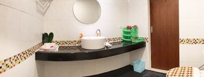 Un bagno con un lavandino bianco, uno specchio e un piano d'appoggio nero. Si notano cesti verdi e un cestino della spazzatura blu.