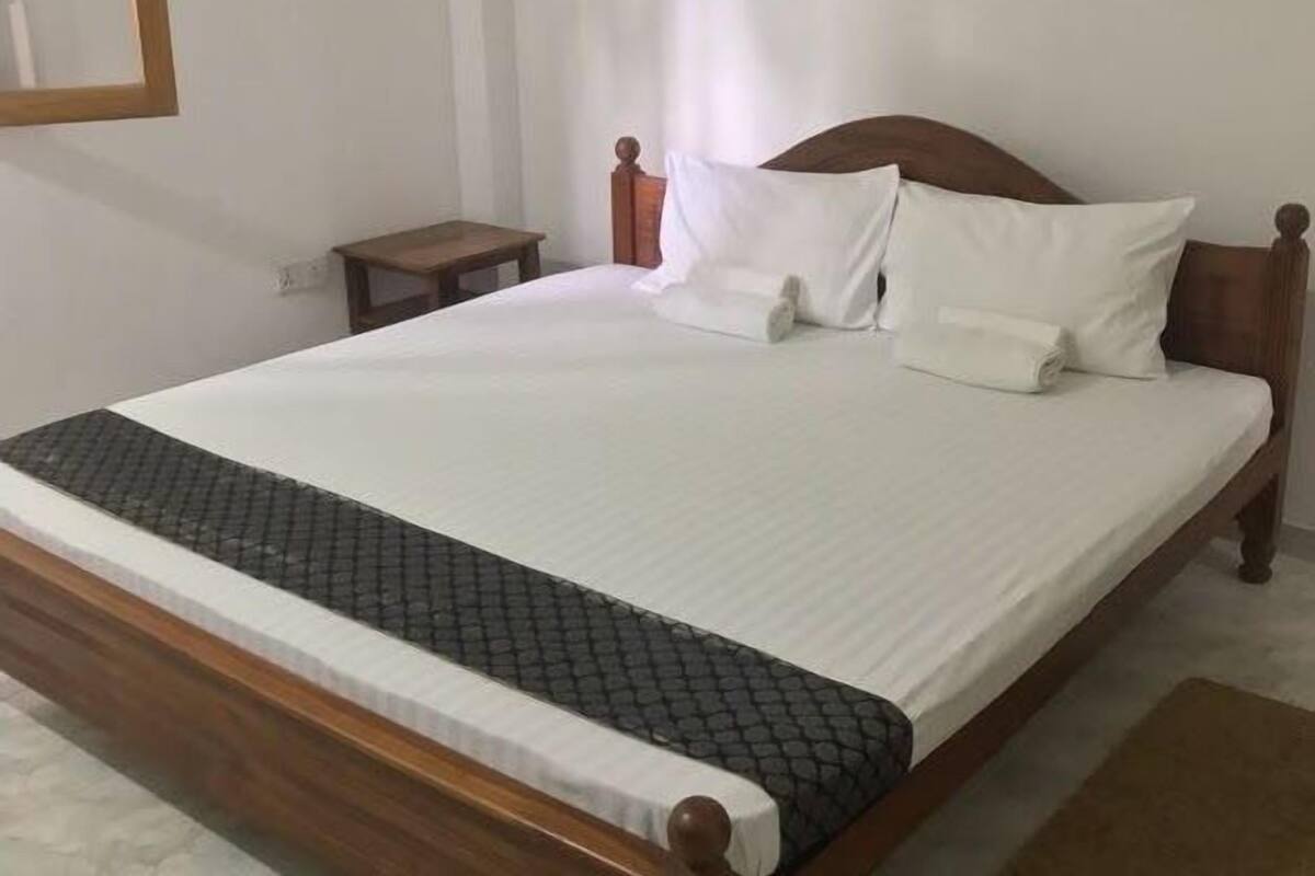 Uma cama bem arrumada com estrutura de madeira, roupa de cama branca e colcha estampada escura.