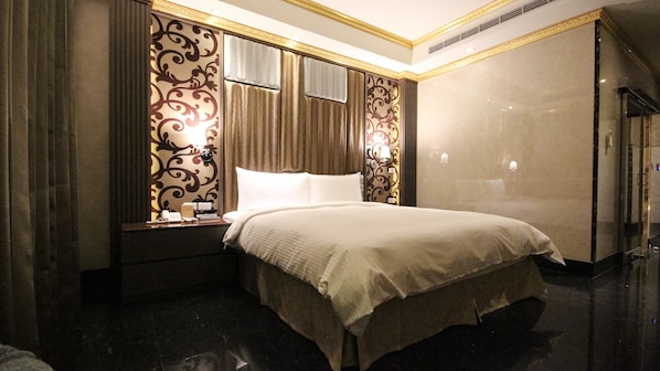 A hotel room with a large bed, a nightstand with a lamp, and a mirror with ornate designs. - Goldsand Hotel (Hsinchu)