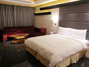 Ein Hotelzimmer mit einem großen Bett, einem roten Sofa, einem kleinen runden Tisch und einem Nachttisch mit Telefon und Lampe.