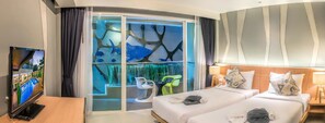 A hotel room with a large TV, a glass partition with a tree design, two beds, and a nightstand with a lamp. - Ratana Patong Beach Hotel by Shanaya (Patong)