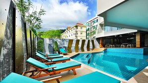 A swimming pool area with lounge chairs and a view of buildings in the background. - Ratana Patong Beach Hotel by Shanaya (Patong)