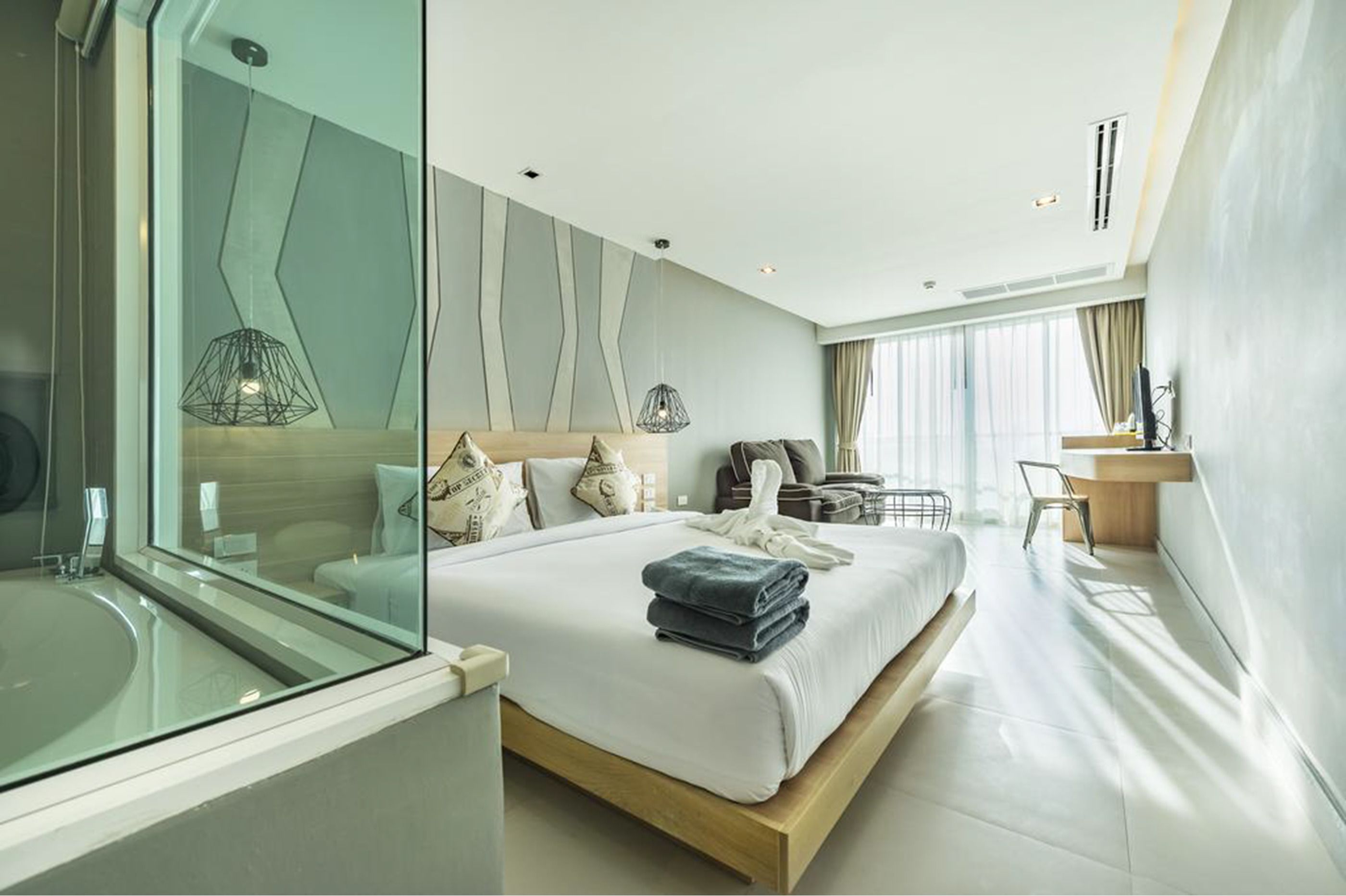 A modern hotel room with a large bed, a glass-enclosed bathroom, a desk, and a view of the city.