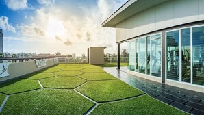 A modern building with a rooftop garden featuring hexagonal grass patterns and a glass facade. - Ratana Patong Beach Hotel by Shanaya (Patong)