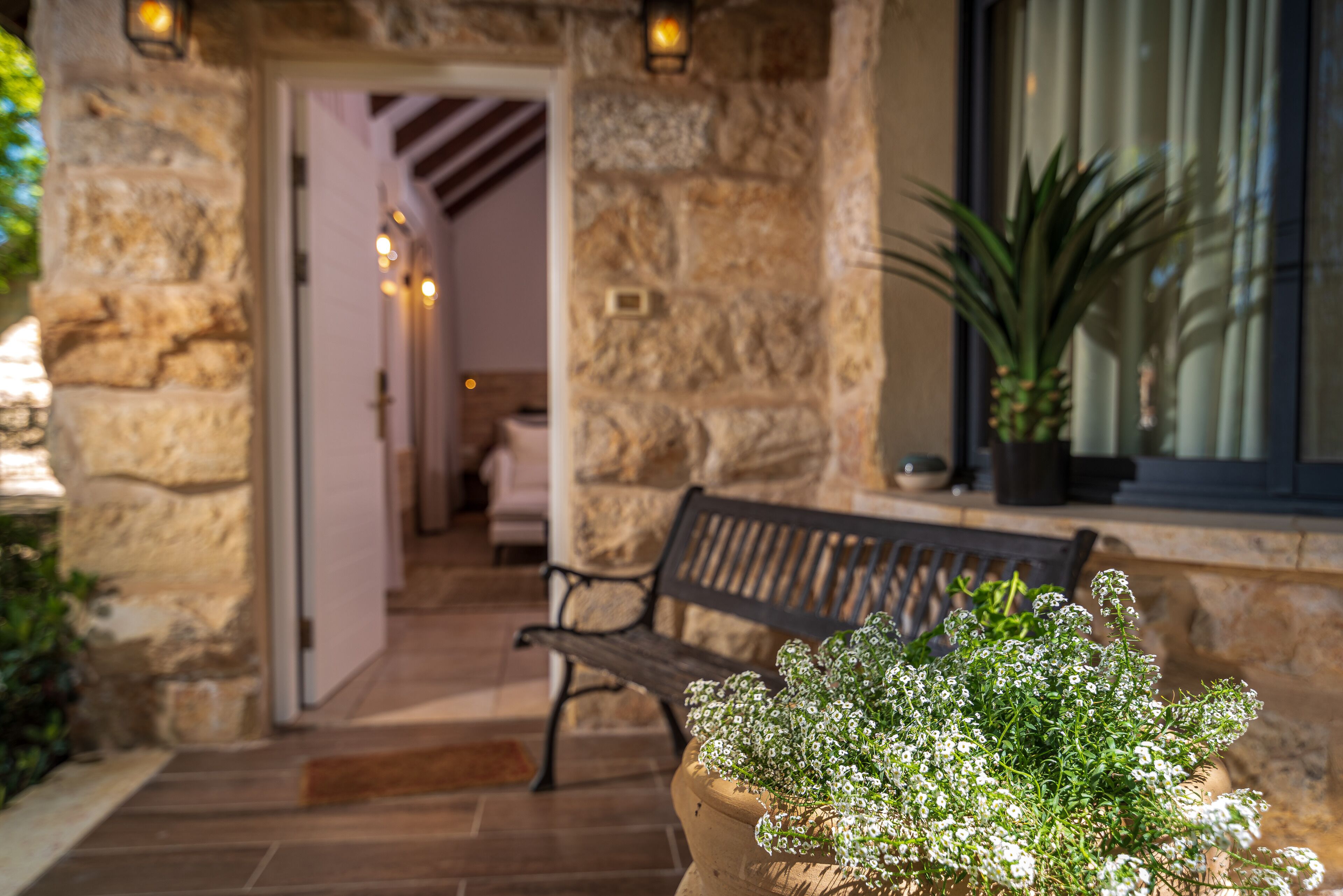 Une façade en pierre, un banc en bois et un pot de fleurs.