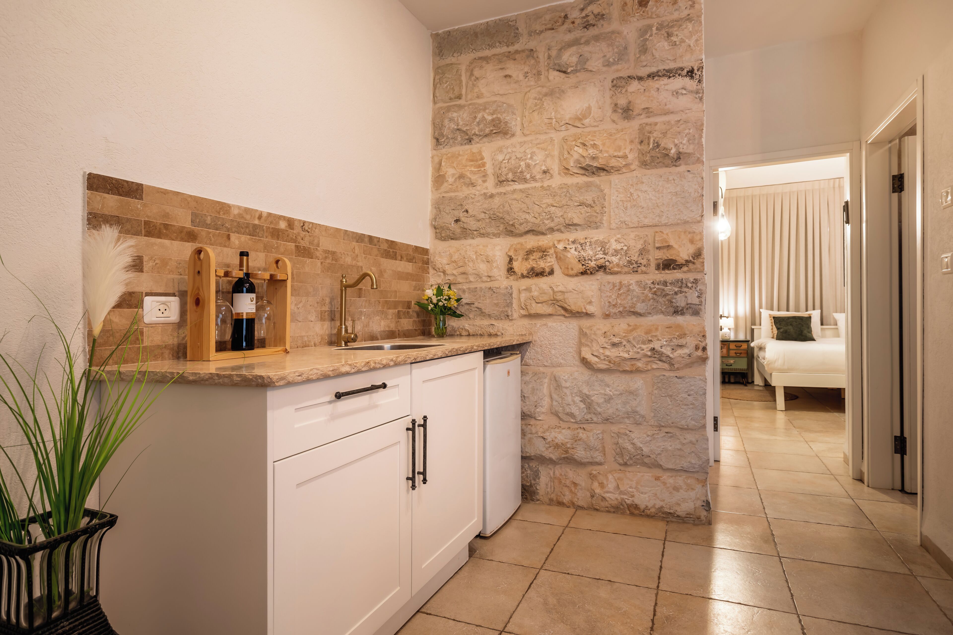 Una cocina moderna con armarios blancos, una pared de acento de piedra y una encimera con botellas de vino y un florero.