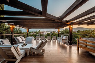 Un espacio al aire libre techado con vigas de madera, sillas blancas acolchadas y una mesa con planta en maceta.