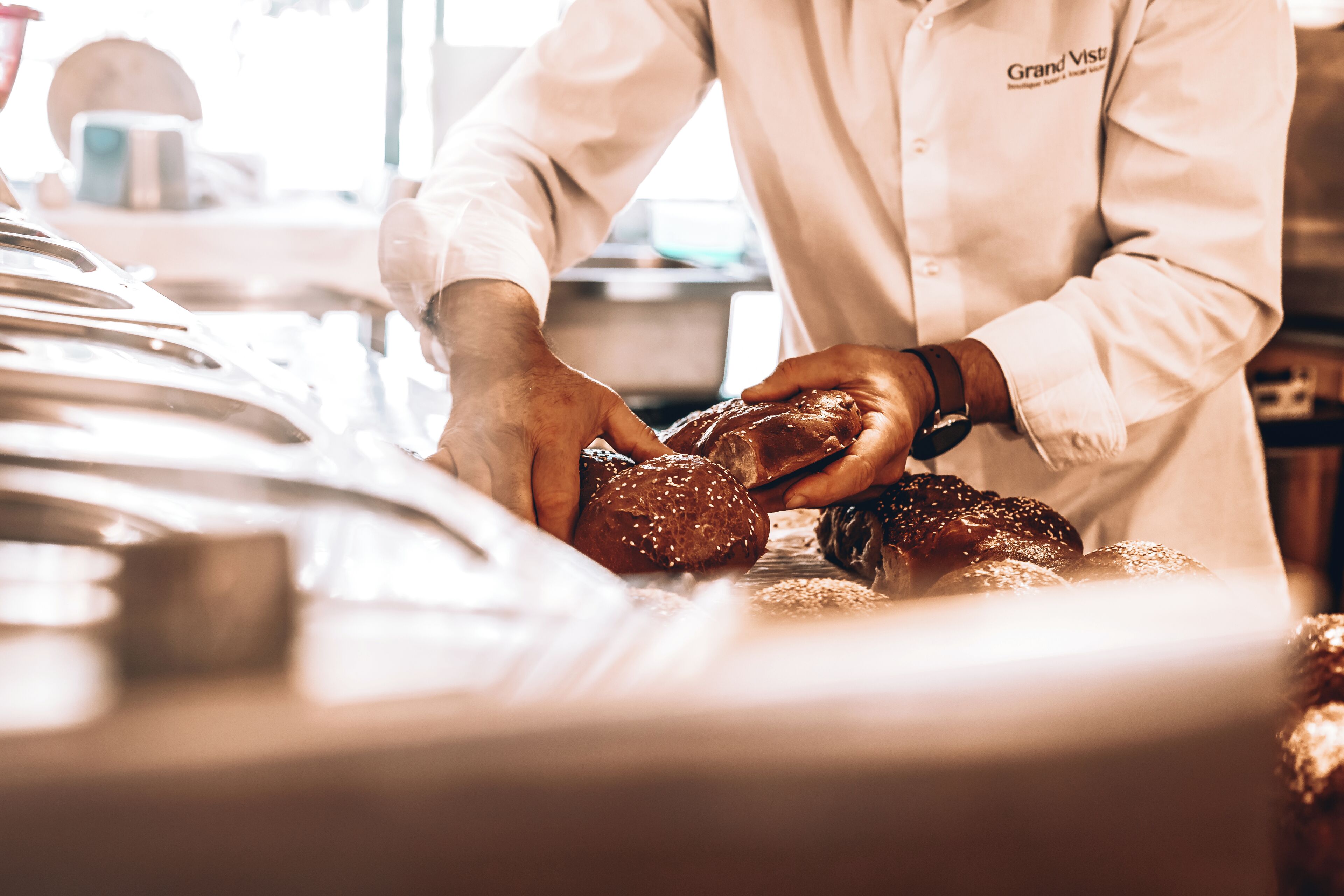 Une personne vêtue d’un uniforme blanc, portant une étiquette avec son nom, manipule un gros morceau de viande, probablement pour le préparer à la cuisson.