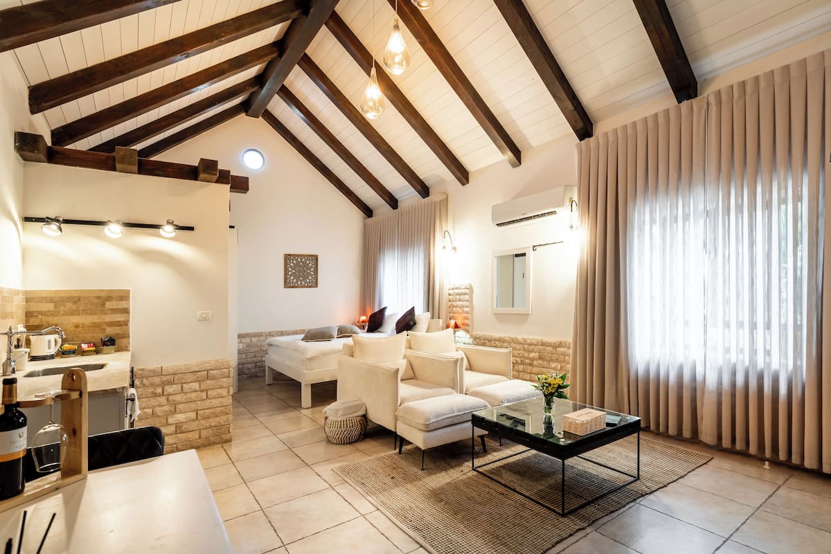 A spacious living area with a high ceiling, a sofa set, a coffee table, and a kitchen area with a sink and countertop.