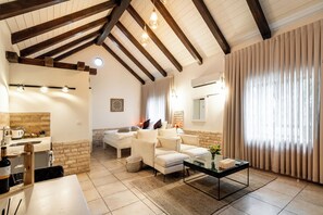 Een ruime woonkamer met een hoge plafond, een zithoek, een salontafel, en een keuken met een spoelbak en aanrecht.