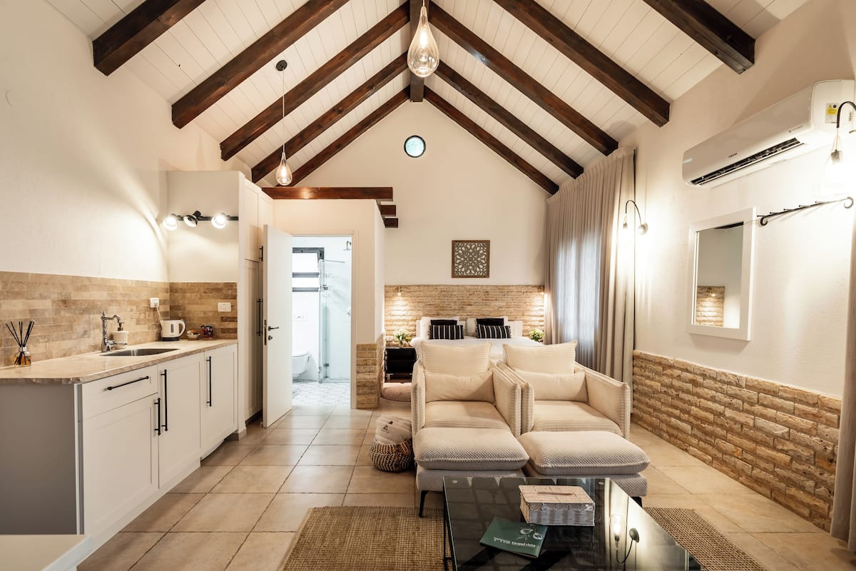 A spacious kitchen with white cabinets, a wooden ceiling, and a dining area with a sofa and table.