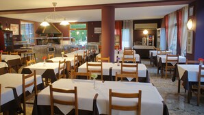 A restaurant with multiple tables and chairs, a kitchen area, and a view of the outdoors. - Hotel la Planada (Ordino)
