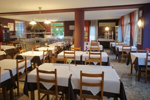 Un restaurante con varias mesas y sillas, una zona de cocina y vistas al exterior.