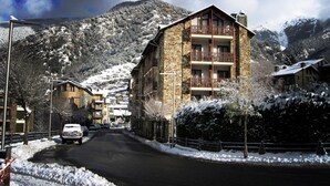 A snow-covered mountain town with a stone building featuring multiple balconies and a ski slope in the background. - Hotel la Planada (Ordino)