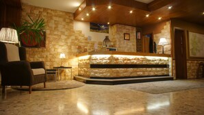 A lobby with a stone reception desk, a plush armchair, and a potted plant. - Hotel la Planada (Ordino)