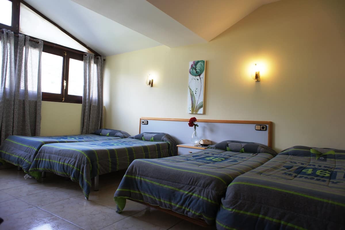 A hotel room with two single beds, a nightstand with a lamp, and a wall-mounted artwork.