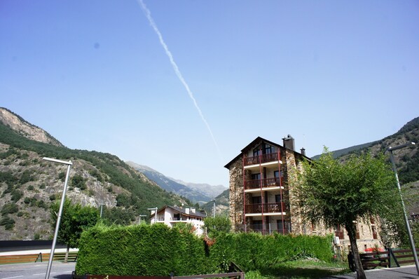 A multi-story building with balconies, surrounded by lush greenery and mountains in the background.