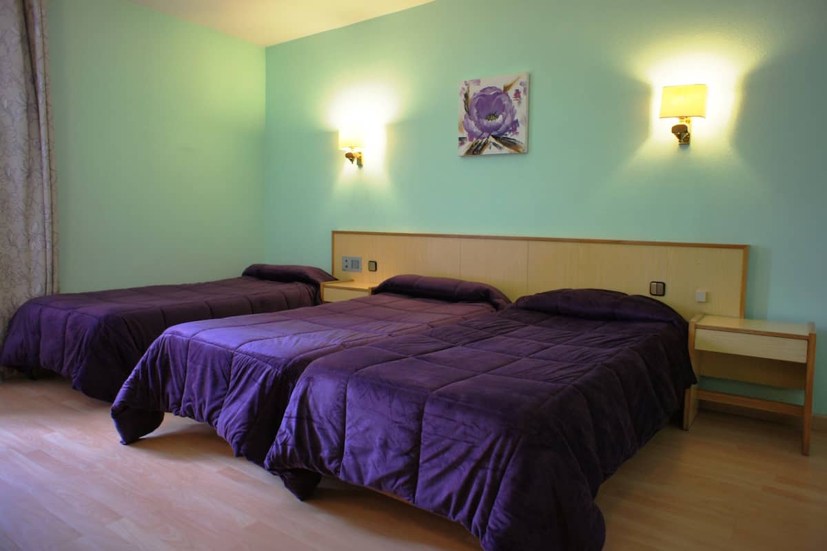 A room with two beds, a nightstand, and a wall-mounted lamp.
