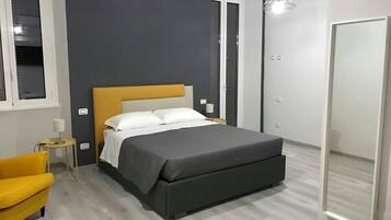 A modern bedroom with a bed, a small bedside table, a chair, and a mirror.