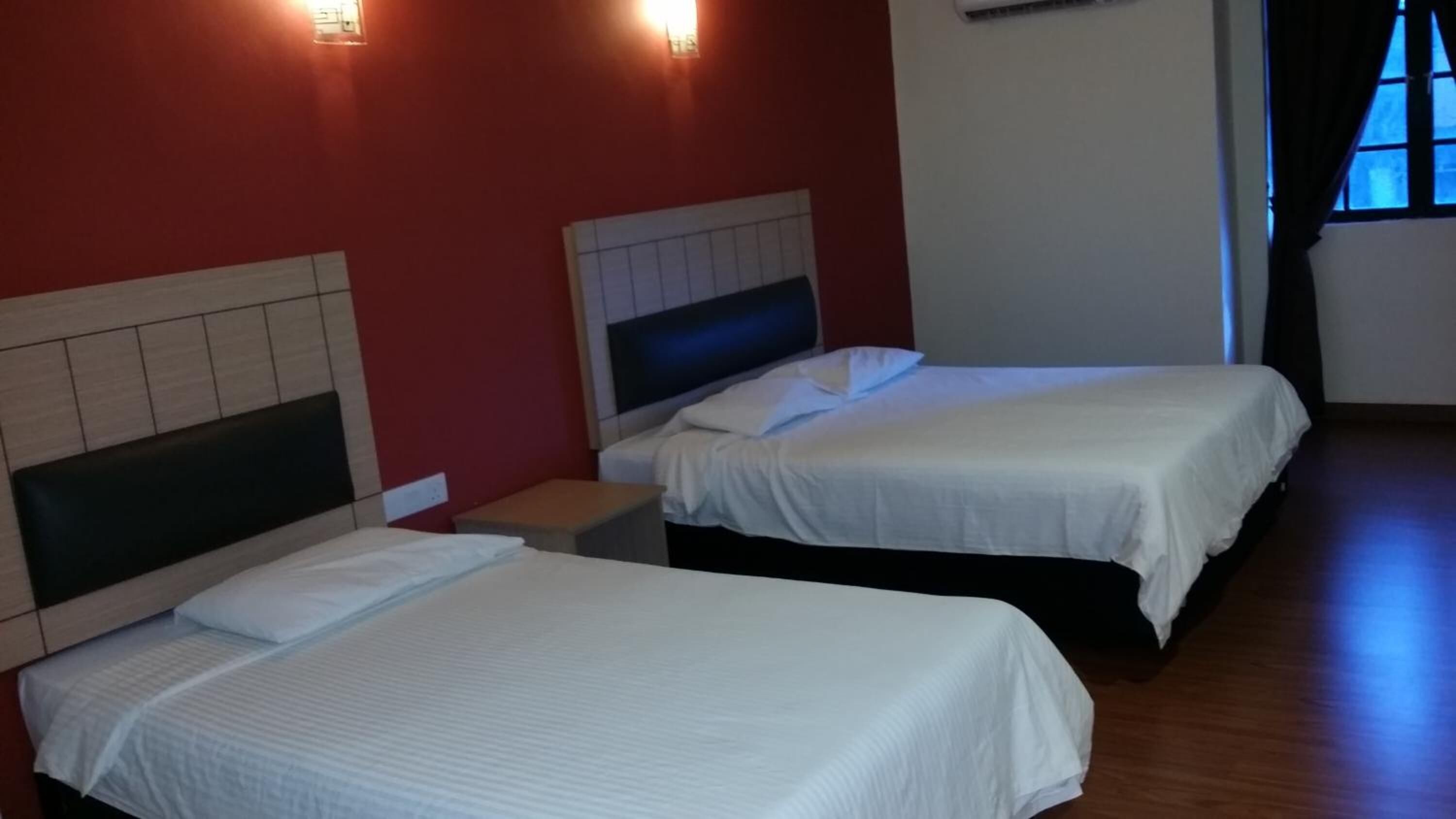 Two single beds with white linens in a room with red walls and a wooden floor.
