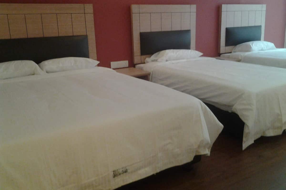 Habitación de hotel con tres camas individuales, cada una con cabecero de madera y ropa de cama blanca.