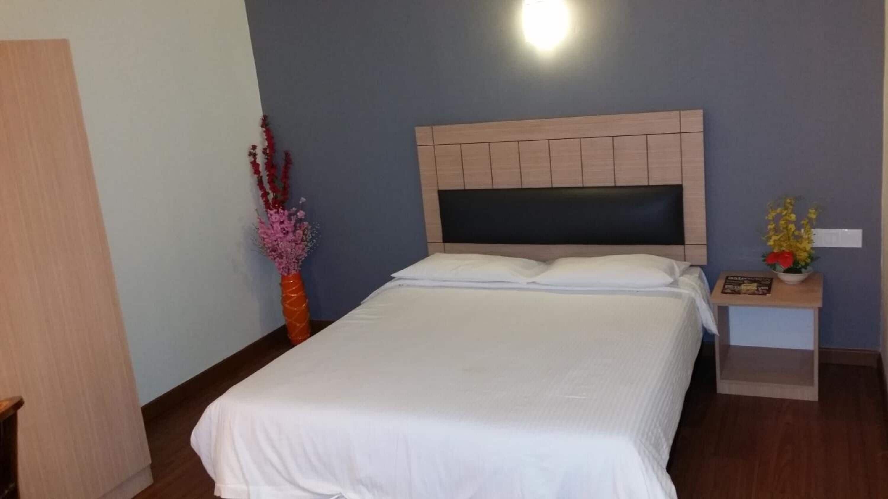 A neatly made bed with a wooden headboard, a bedside table with a lamp, and a vase with flowers.