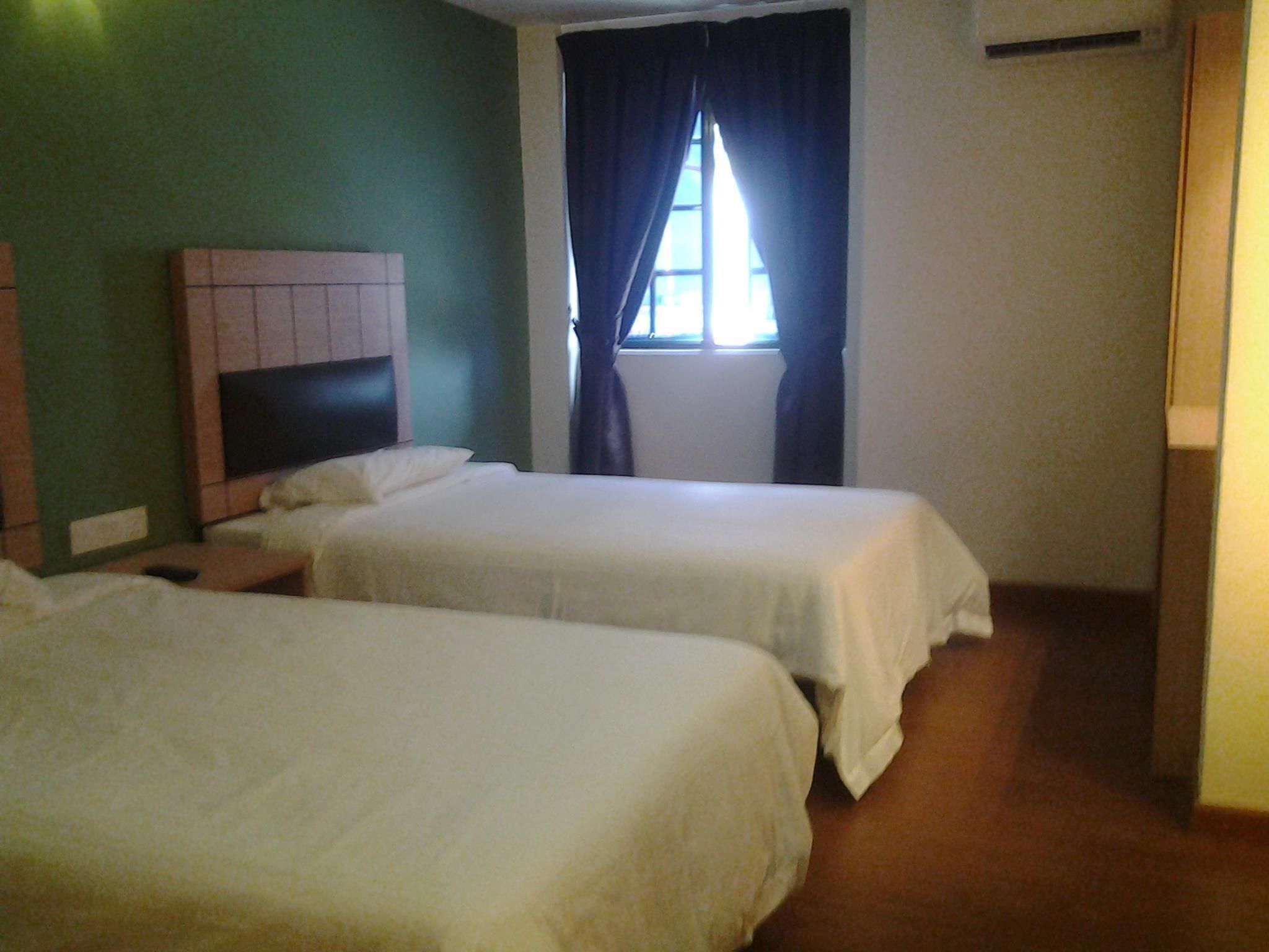 A room with two single beds, a headboard, a window with curtains, and a wall-mounted air conditioning unit.