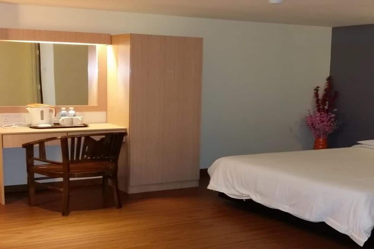 Habitación de hotel con un escritorio de madera, una silla, una cama y una mesita de noche con un jarrón de flores.