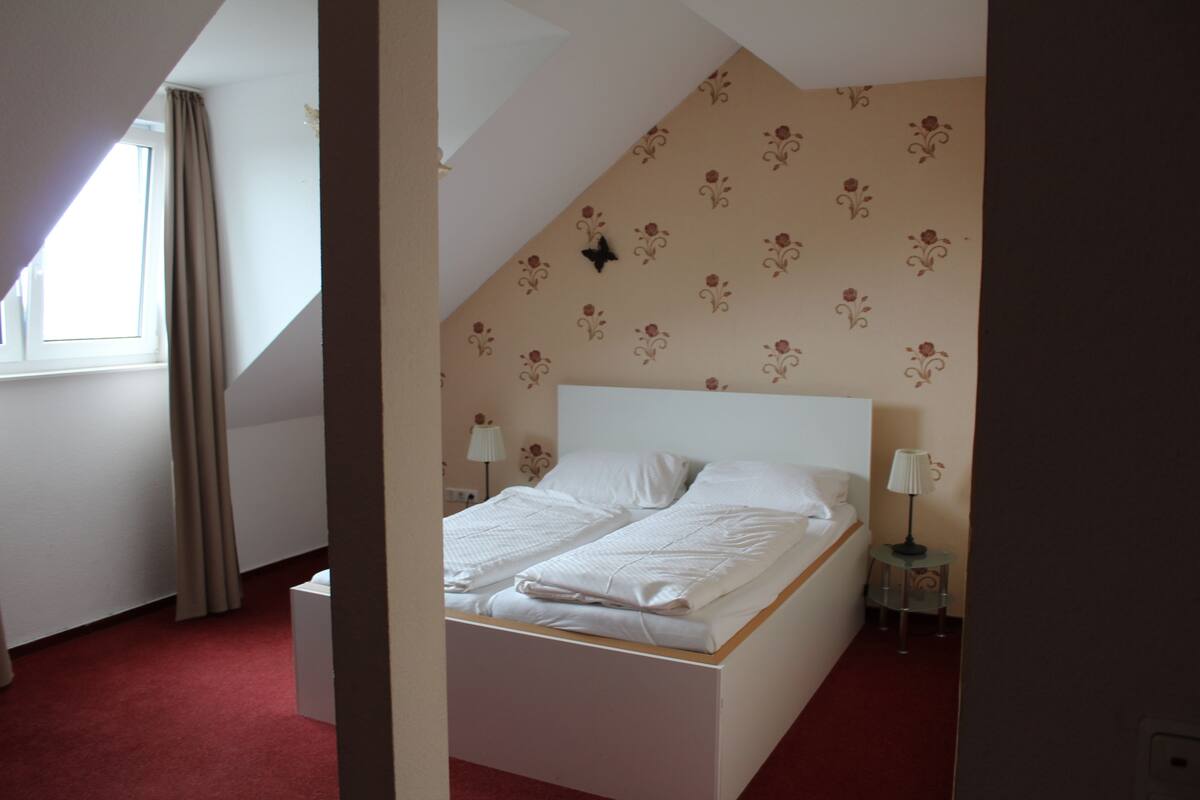 A bedroom with a bed, two bedside tables, a window with curtains, and a floral-patterned wall.