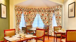 Comedor con cortinas florales, muebles de madera y cuadros en las paredes.