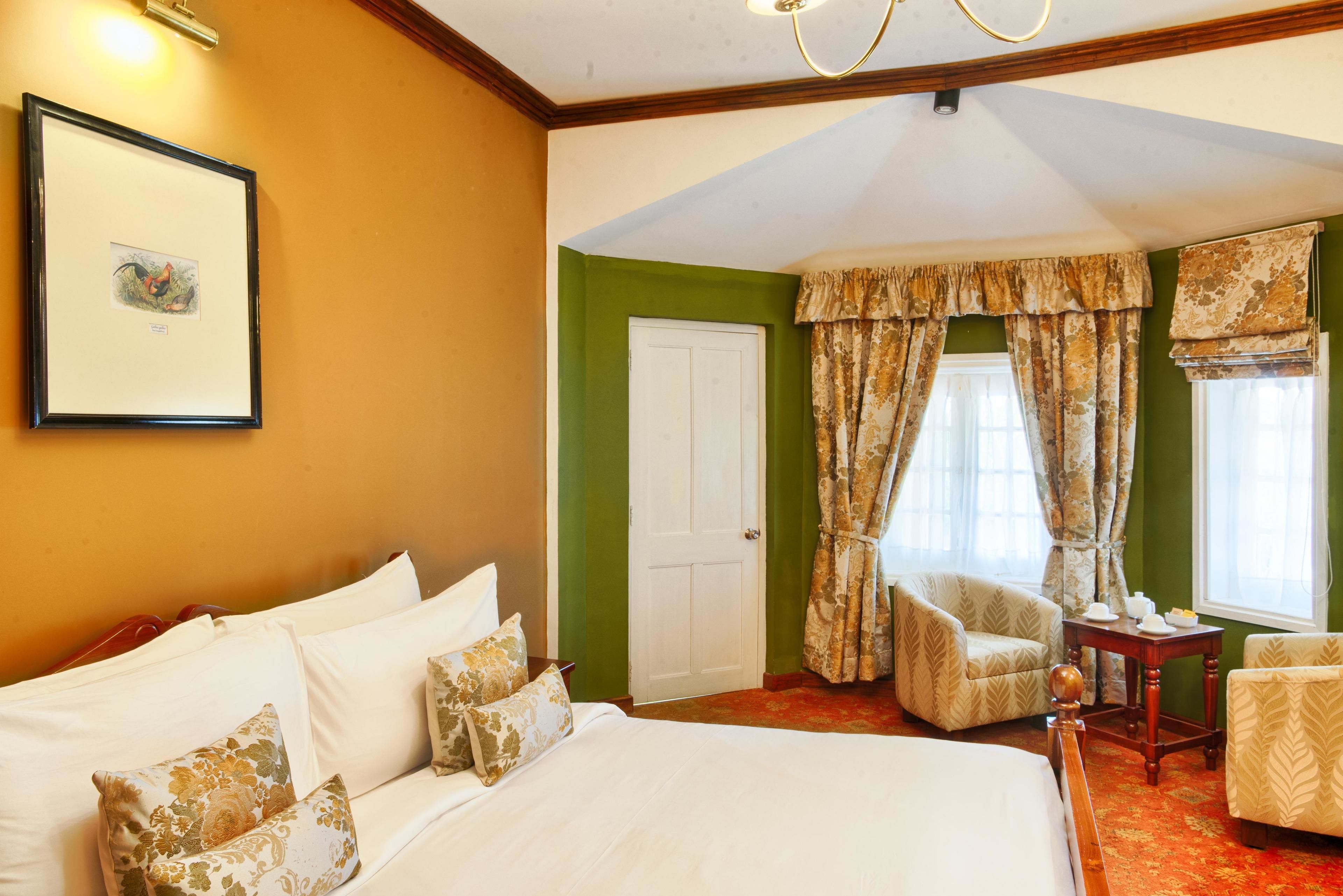 A hotel room with a large bed, a chair, a small table, and a window with curtains.