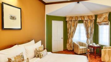 A hotel room with a large bed, a chair, a small table, and a window with curtains.