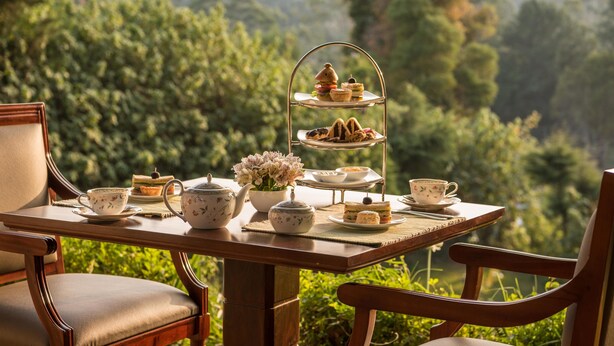 Un juego de té de tres niveles sobre una mesa de madera al aire libre, con un exuberante fondo verde.