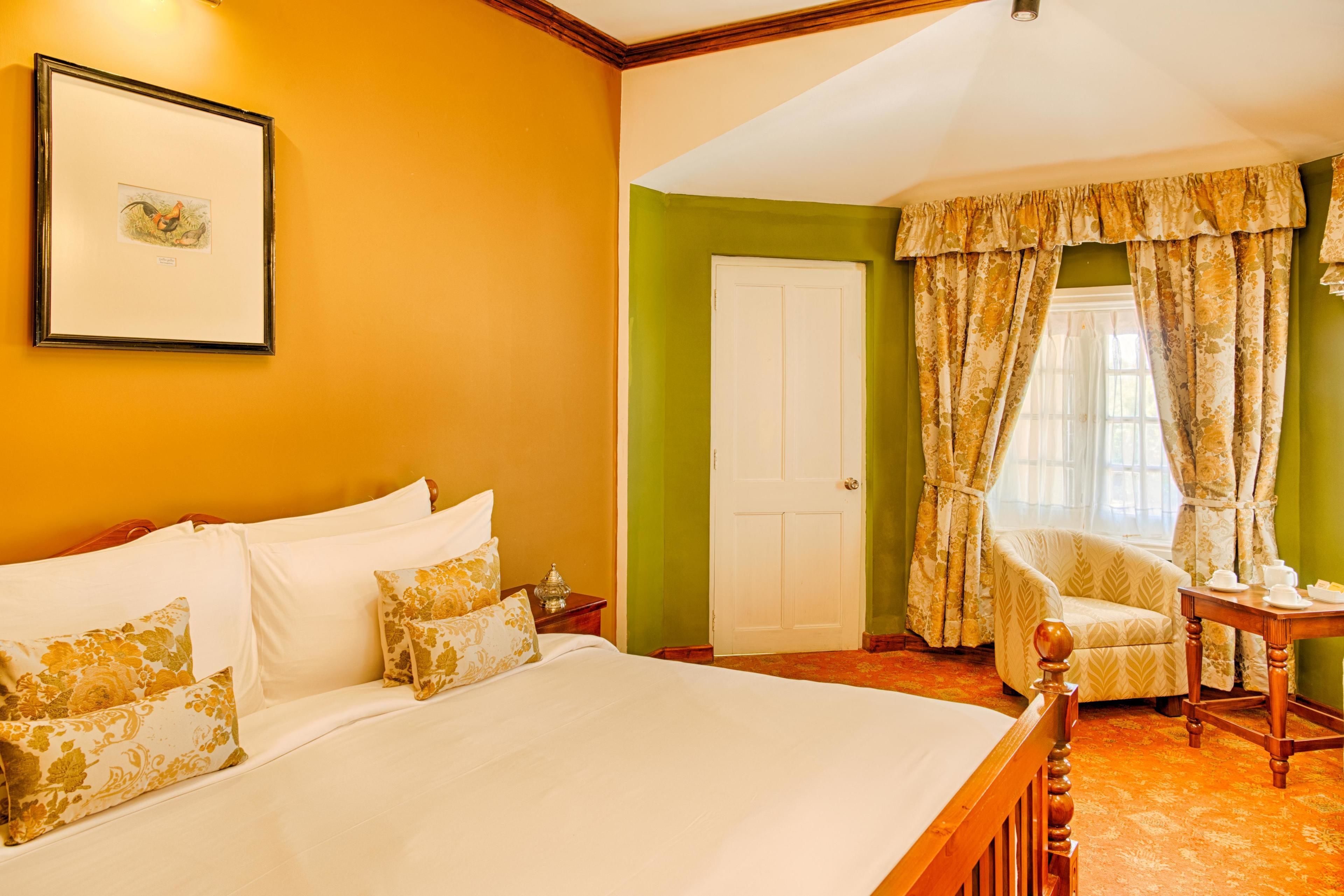 A hotel room with a large bed, a chair, a table with cups, and a framed picture on the wall.