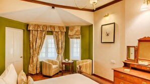 Habitación de hotel con una cama grande, dos sillones, una mesita, un aparador y una ventana con cortinas.