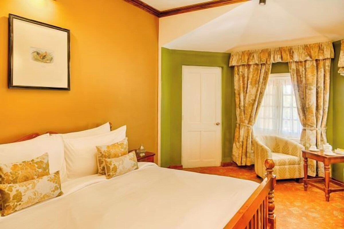 A hotel room with a large bed, a chair, a table, and a door.