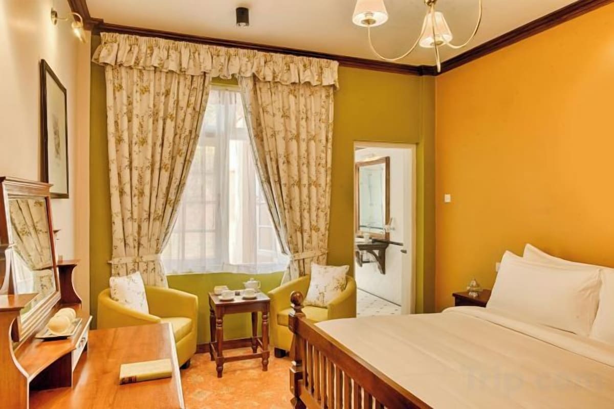 A hotel room with a bed, a chair, a small table, and a window with curtains.
