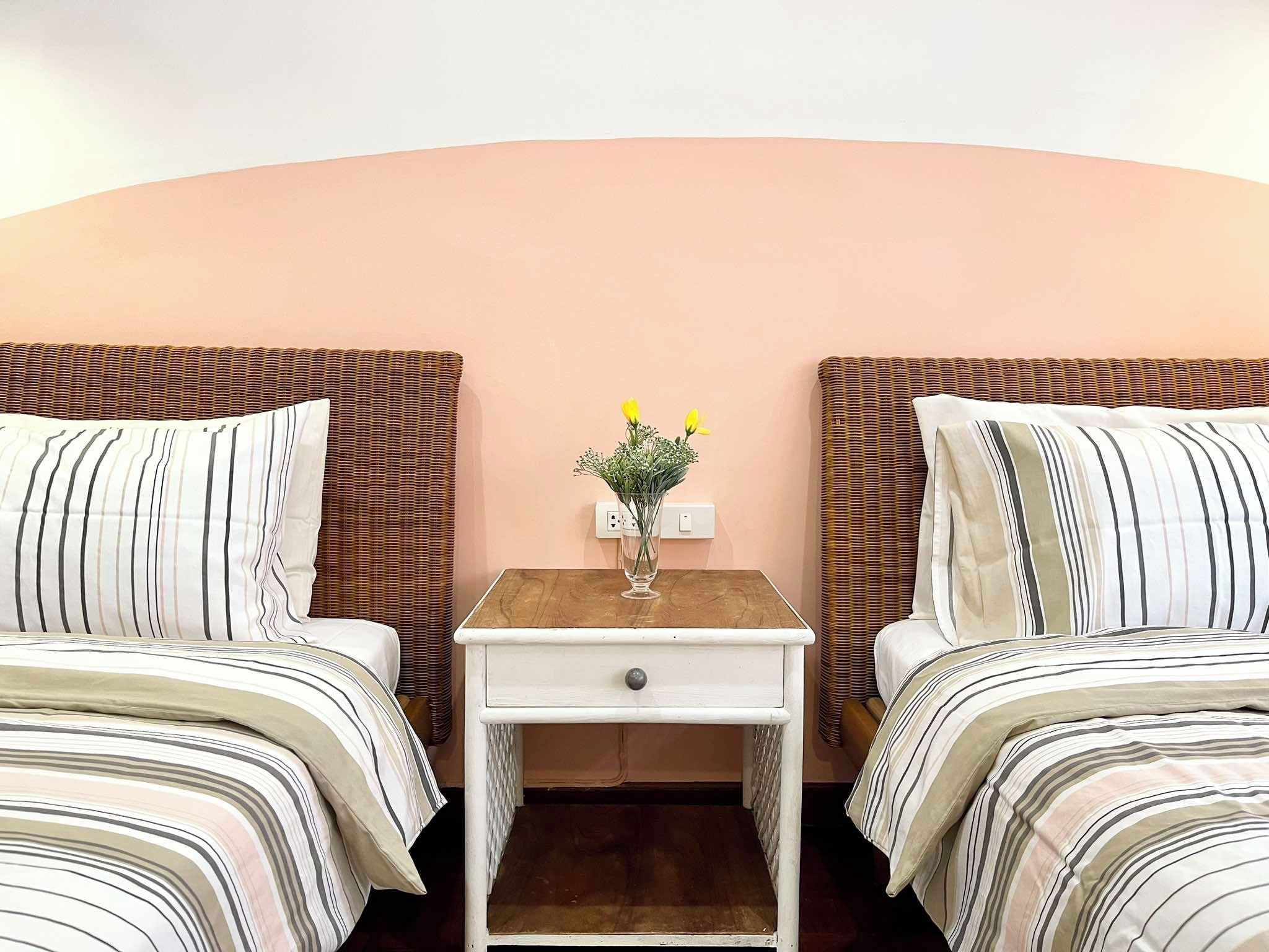 Una habitación de hotel con dos camas, una mesita de noche con un florero y una pared lisa.
