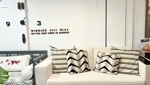 A living room with a sofa, pillows, a small table, and a wall with a clock and a sign. - Winnine Cozy Home (Bangkok)