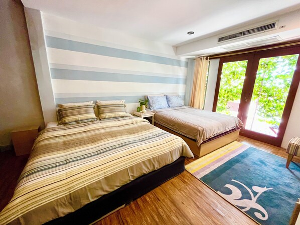 A bedroom with two beds, a window with curtains, and a wooden floor.